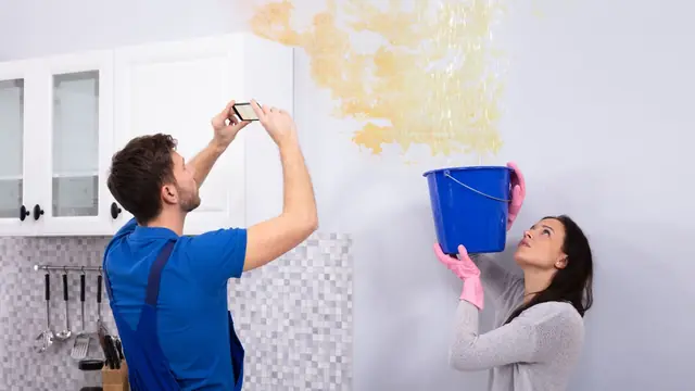 Homeowner photographing a water-stained wall while another person holds a bucket
