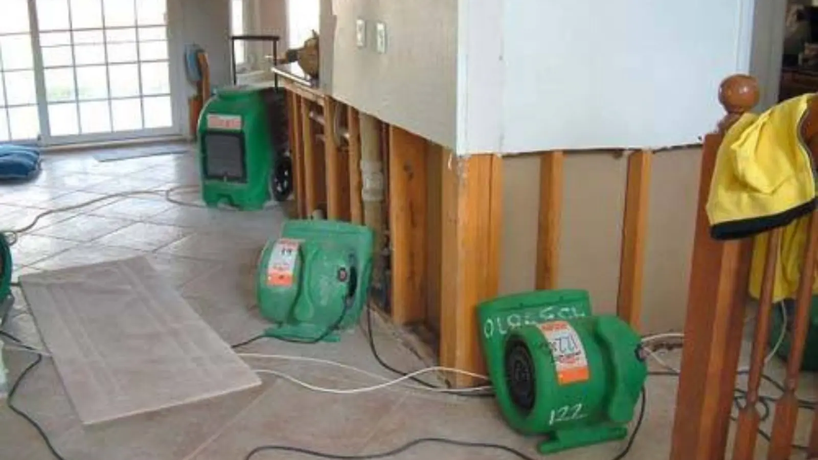 Green air movers running next to an opened wall cavity in a water-damaged room
